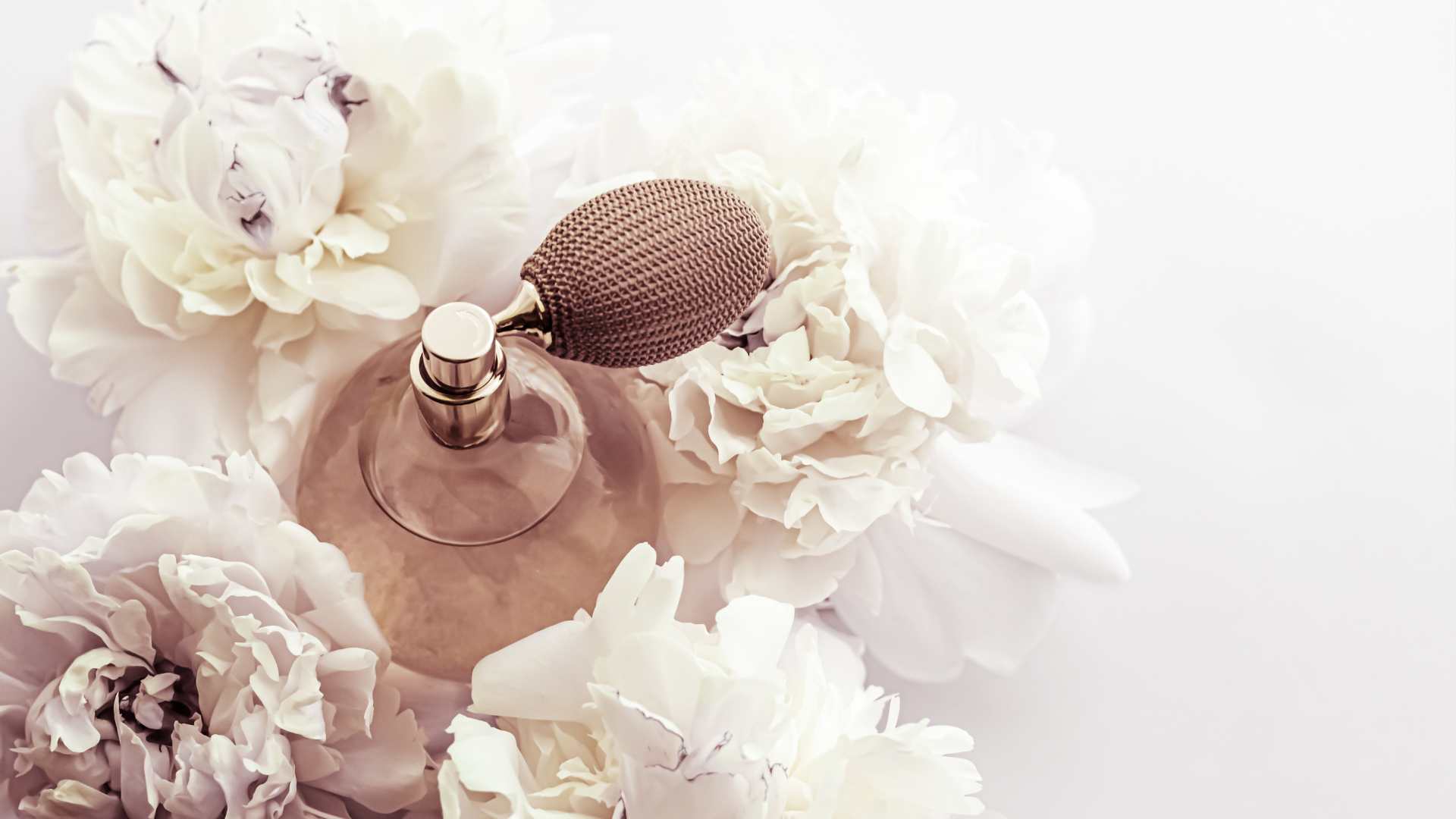 Glass perfume atomizer among pale flowers